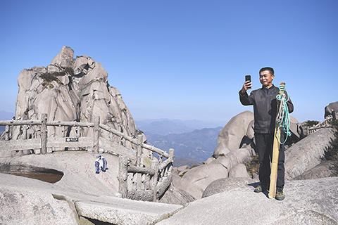 ◎ 十一月十三日,徐勝利在天池峰上拍攝視頻。每次送貨到達峰頂後,徐勝利喜歡拿手機記錄天柱山的風光並在朋友圈分享。(新華社記者劉軍喜攝)