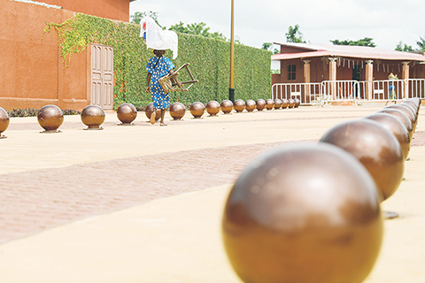 ◎ 五月廿七日,在貝寧維達,一名女子走過查查廣場。地上的圓球形裝飾物象徵著在此地被販賣的奴隸。(新華社記者李亞輝 攝)