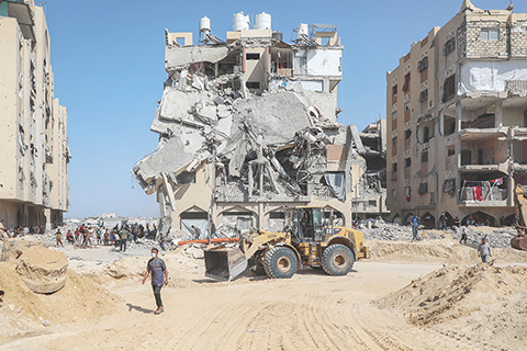 ◎ 十月十七日,司機駕駛裝載機在加沙地帶汗尤尼斯清理街道,搜尋遺體。巴勒斯坦伊斯蘭抵抗運動(哈馬斯)近日重申,仍致力於履行停火協議,但需要一定時間才能移交所有遺體,緣由是一些遺體被埋在遭以軍摧毀的地道裡,以及遭以軍轟炸建築的廢墟中。要找到這些遺體,以方必須允許重型機械和挖掘設備進入加沙地帶。(新華社發 裡澤克.阿卜杜勒賈瓦德 攝)
